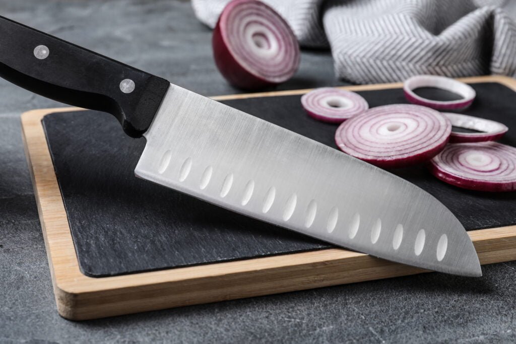 Board with sharp knife and cut onion on grey background
